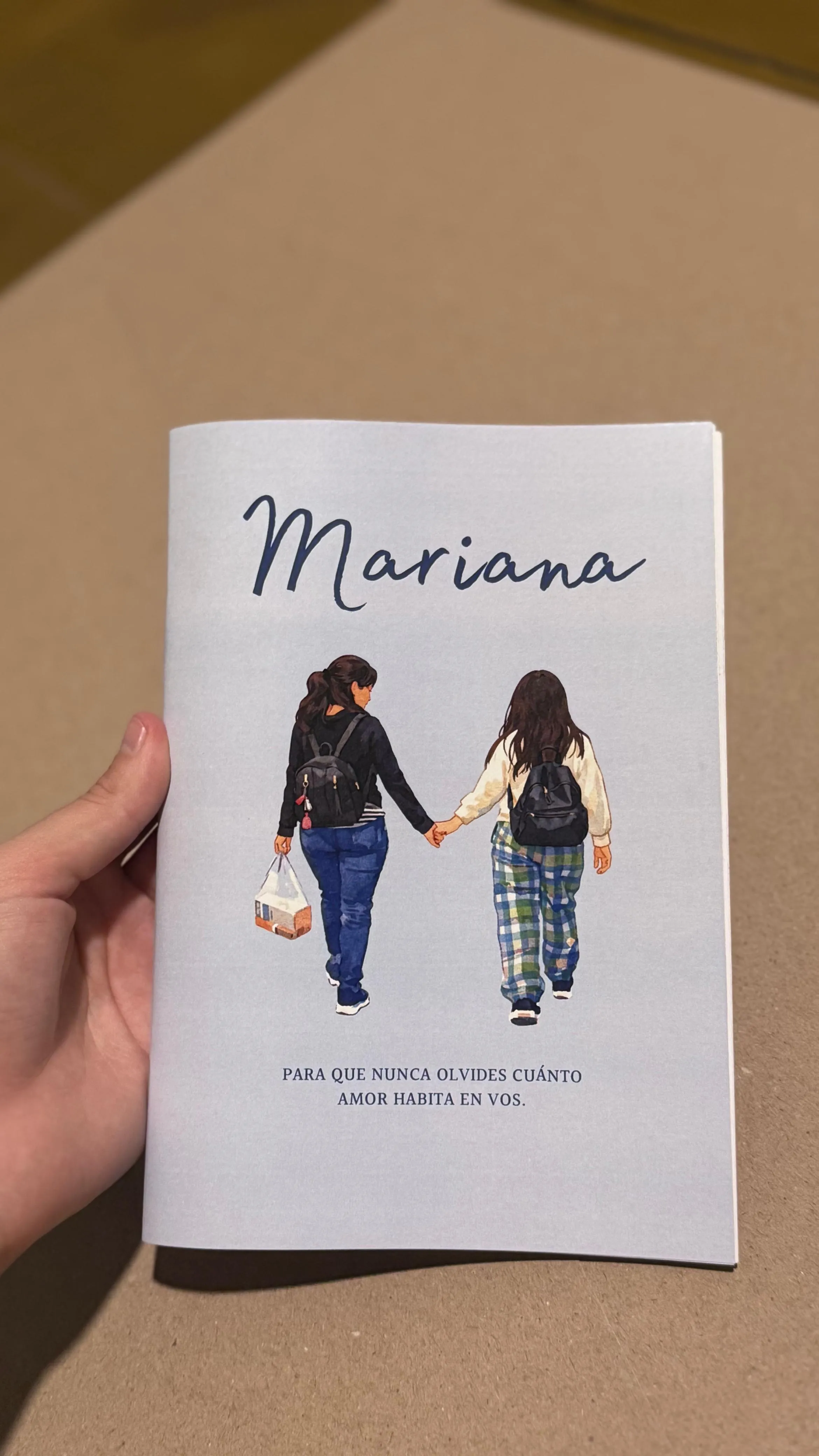 Fotolibro de tapa blanda con la portada ilustrada de dos mujeres caminando de la mano, sobre una mesa de madera